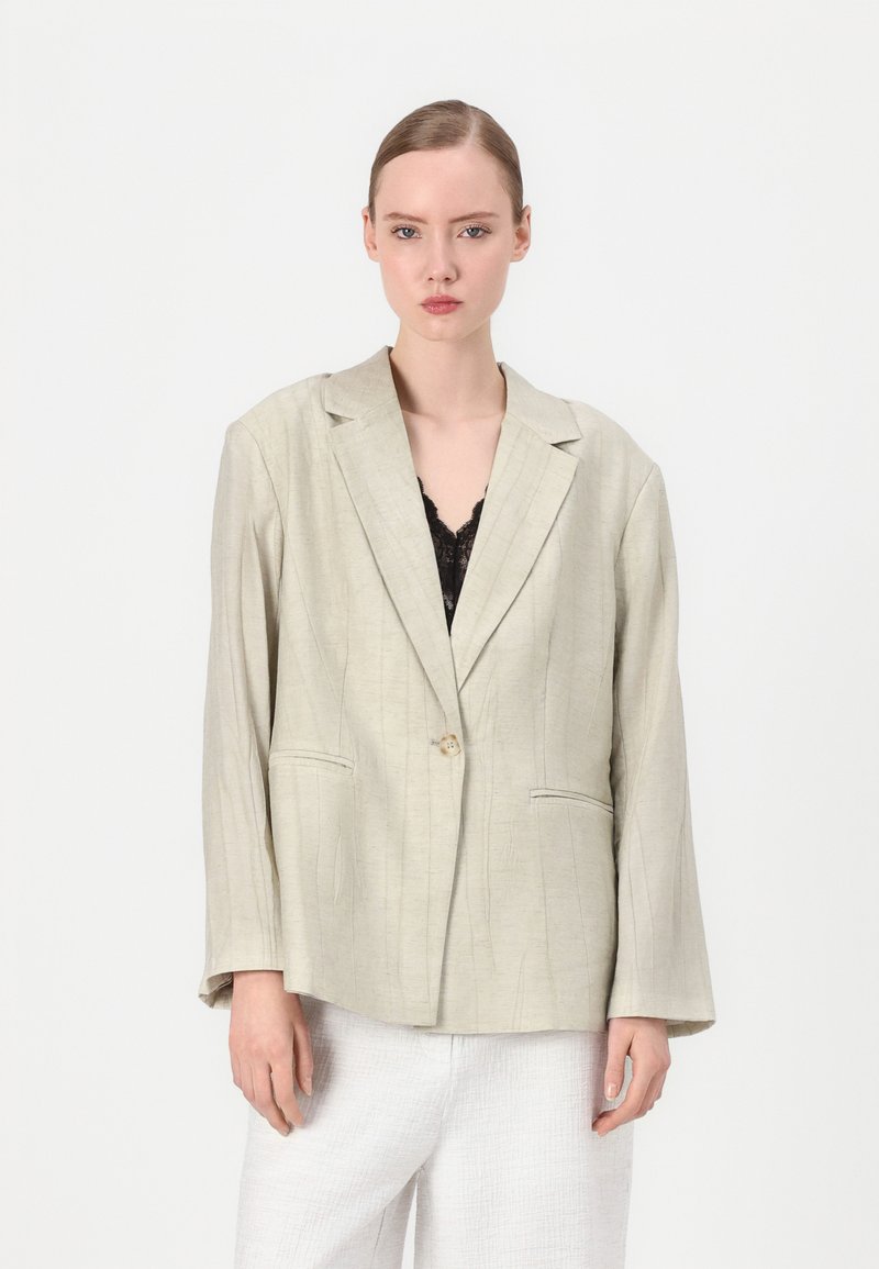 Beige lina bleiser, mille madal krae, ühe nupuga kinnitamine ja eesmine taskud. Selles on peened vertikaalsed triibud ja pikad küllused.