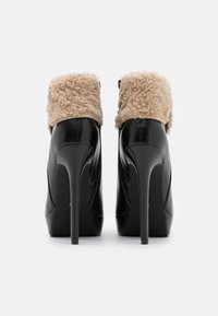 Stivali neri con tacco alto, dotati di un morbido colletto in pelliccia sintetica beige, caratterizzati da un design elegante, una texture in pelle liscia e punta affusolata.