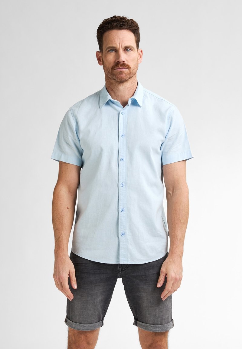 Cămașă cu mânecă scurtă, cu nasturi, de culoare albastru deschis, cu guler, confecționată dintr-un material ușor. Asortată cu pantaloni scurți gri închis, cu margini rulate.