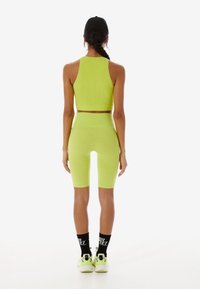 Neon-grüner, gerippter Sport-BH und passende, hoch taillierte Biker-Shorts, kombiniert mit schwarzen Socken und Turnschuhen, von hinten gesehen.