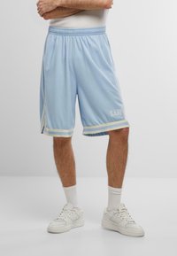 Gaiši zili basketbola šorti ar baltām un bežām svītrām ap apakšmalu, elastīga jostasvieta un izšūts "KANI" logo kreisajā pusē.
