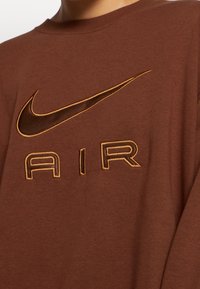 Sudadera marrón hecha de una tela suave, con un logo de Nike en relieve y "AIR" en un bordado dorado en contraste. Mangas largas, cuello redondo.