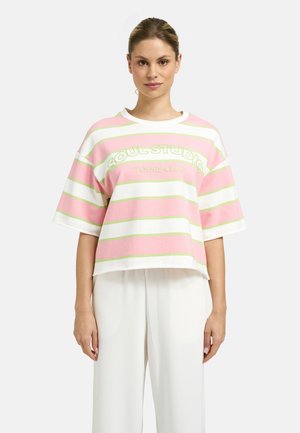 Woman wearing a pastel pink and white striped oversized shirt with "Soul Studio Tennis Club" text, paired with loose white pants.