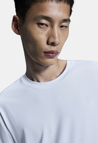 White crew neck t-shirt with smooth texture, minimal design. Model's face partially visible, showcasing short hair and neutral expression.