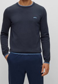 Suéter de punto azul marino con cuello y puños acanalados en azul, que presenta un pequeño logotipo azul "BOSS" en el pecho, combinado con pantalones azul marino a juego.