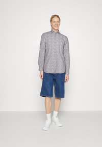 Lichtblauwe gestreepte lange mouwen shirt met een button-down kraag, gecombineerd met donkerblauwe denim shorts en witte sneakers.