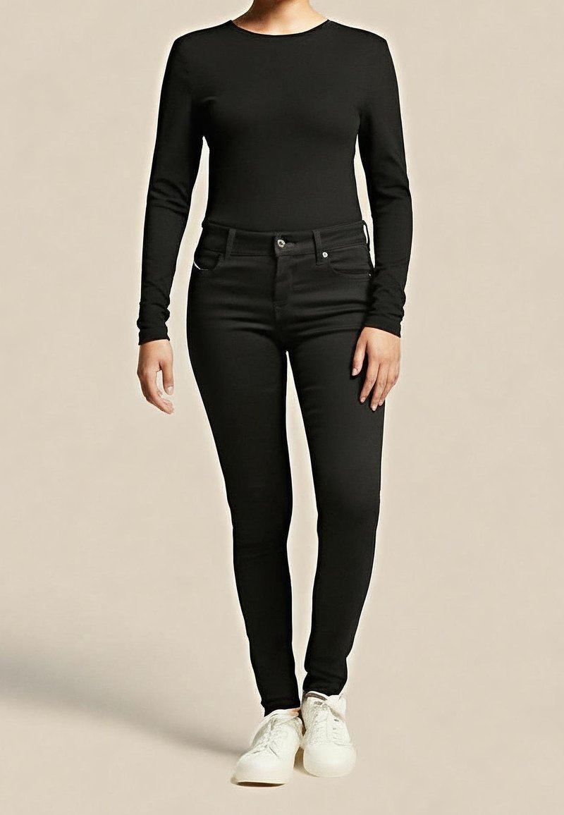 Black long-sleeve top paired with form-fitting black jeans. The outfit features a smooth texture and is complemented by white sneakers.