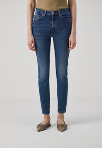 Smal passform blå bukser med lett falmet denim, frontlommer og beltehemper. Kombinert med lysebrune flate sko.