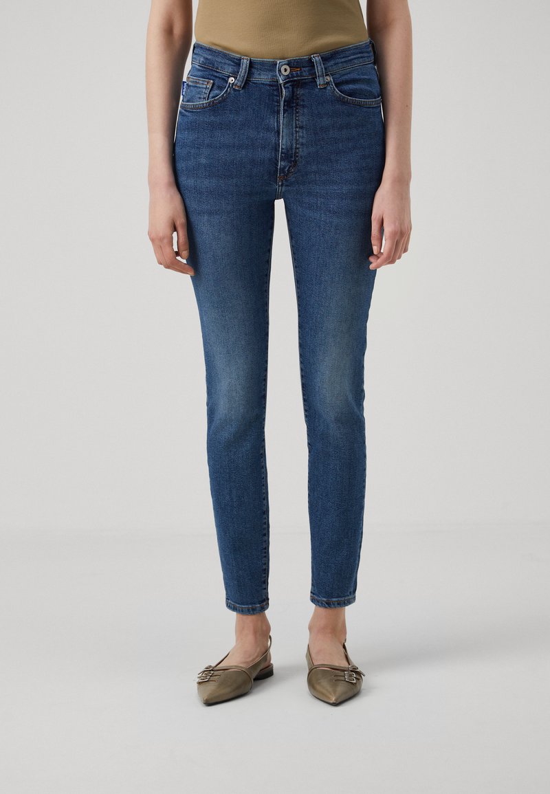 Smal passform blå bukser med lett falmet denim, frontlommer og beltehemper. Kombinert med lysebrune flate sko.