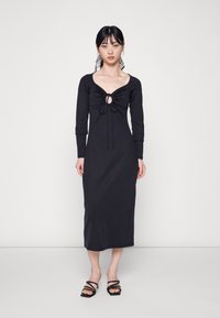 Vestido preto de mangas longas feito de um material macio, apresentando um decote em U com um detalhe franzido e cordão, que se estende até a metade da panturrilha.