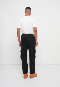 Sorte cargo bukser med elastisk talje, to sidelommer og to store sidelommer, parret med en hvid t-shirt og brune støvler.