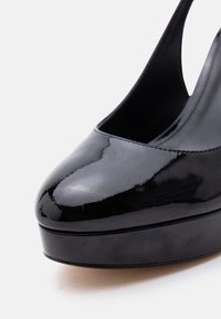 Μαύρο παπούτσι από δερμάτινο πατινένιο υλικό με ψηλό τακούνι, στρογγυλεμένη μύτη και σόλα με πλατφόρμα σε λευκό φόντο.