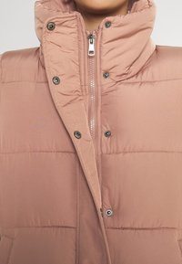 Lichtroze gewatteerde vest met een hoge kraag, rits aan de voorkant en drukknoopsluiting. Glad textuur met een horizontaal gestikt design.