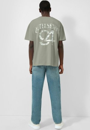 Person wearing a gray oversized T-shirt with “QUOTHSENSE C4” in large, distressed white letters, light blue jeans, and white sneakers, standing facing away.