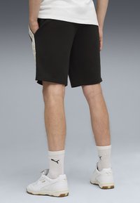 Pantalones cortos deportivos negros con un bolsillo lateral, que presentan un patrón geométrico. Llevados con zapatos blancos y calcetas de color claro con textura acanalada.