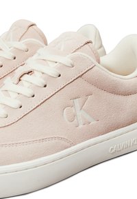 Világos rózsaszín velúr sportcipők fehér fűzőkkel, texturált felülettel, valamint dombornyomott "CK" és "CALVIN KLEIN" márkajellel az oldalán.