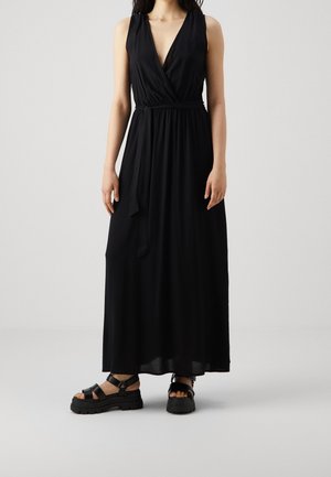 Czarna długa sukienka bez rękawów z głębokim dekoltem w serek i regulowanym paskiem w talii. Do tego masywne czarne sandały z grubymi paskami.