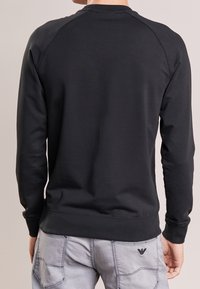 Black crewneck sweatshirt with long sleeves, ribbed cuffs and hem, made of smooth fabric, featuring a subtle logo on the upper back.