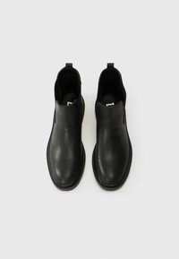 Botas de cuero negro hasta el tobillo con una textura suave, puntera redonda y paneles laterales elásticos. Diseño minimalista con una suela contrastante.