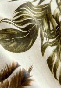 Material textil cu fundal crem și modele de frunze verzi și maro. Țesătura are un aspect moale, texturat, cu un aspect natural.