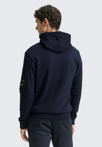 Navyblauwe hoodie met een gestructureerde afwerking, opvallende stiksels en een klein label op de linkermouw.