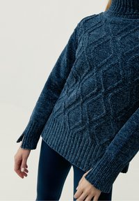 Mörkblå stickad tröja med ett strukturerat diamantmönster, ribbad krage och manschetter, sidofickor och ett mjukt, mysigt utseende.