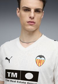 Jersey de fútbol blanco con un patrón texturizado, logo negro de Puma en el hombro izquierdo y un colorido escudo del Valencia C.F. en el pecho.