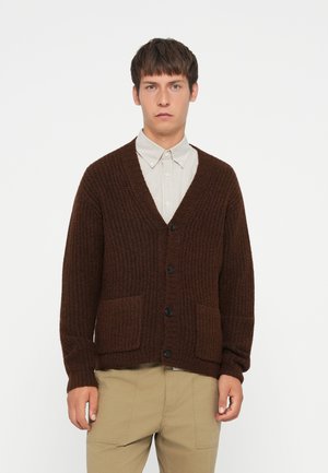 Brown, knitted cardigan with a deep V-neck, front pockets, and black buttons. Features a textured fabric and relaxed fit. Worn over a striped shirt.