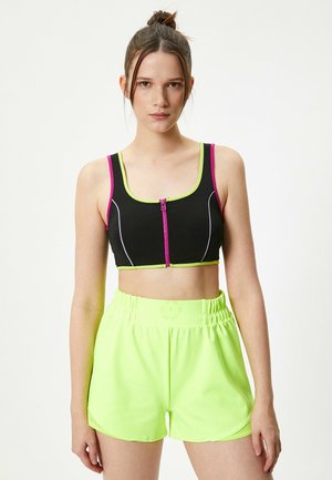 Top corto negro con acentos en rosa y verde, con un cierre frontal. Pantalones cortos neón verdes con cinturilla elástica y textura suave.