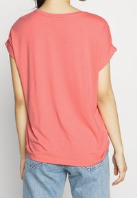 Korallfärgad bomullströja med korta, rullade ärmar, avslappnad passform och rundad halsringning. Bärs tillsammans med ljusblå denimjeans.
