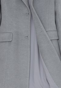 Blazer grigio chiaro realizzato in tessuto testurizzato, con due tasche frontali e design monopetto. Fodera interna visibile.