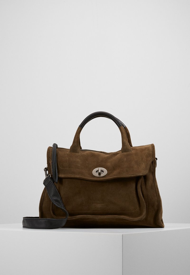 Sac à main en daim marron avec une poignée et une bandoulière en cuir noir, doté d'un rabat avant avec un fermoir à verrou tournant argenté, posé sur une surface blanche.