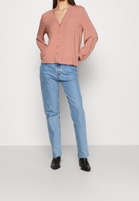 Chemise rose poussiéreux à boutons avec un décolleté en V et des manches longues, associée à un jean droit bleu clair et des bottines noires.