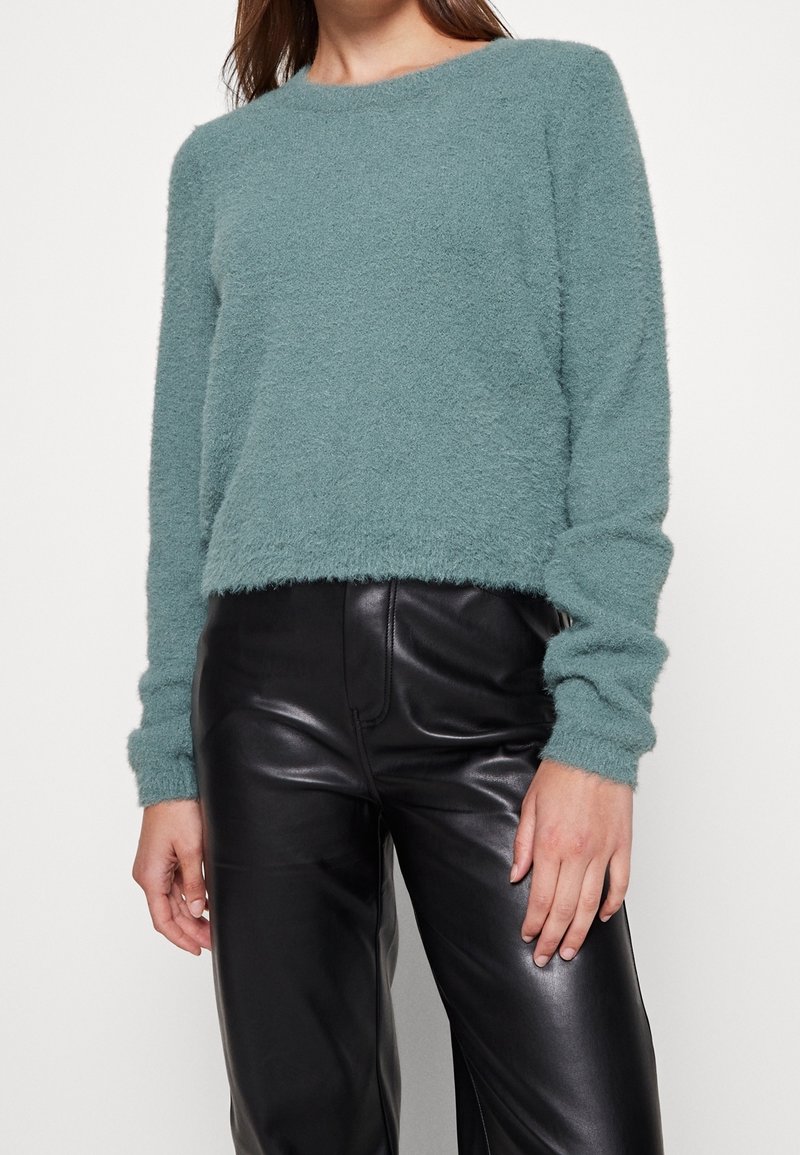Camiseta de punto esponjosa verde menta con cuello redondo y mangas largas, combinada con pantalones de cuero negros de tiro alto, de textura suave.