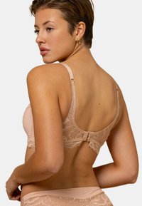 Soutien-gorge en dentelle beige doux avec bretelles réglables et fermeture à crochet ; présente des motifs floraux et un tissu lisse pour le confort.