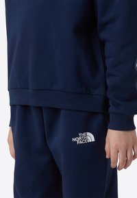 Marineblå genser og matchende joggebukser laget av mykt stoff. Har ribbede mansjetter og kant, med en hvit logo på benet.