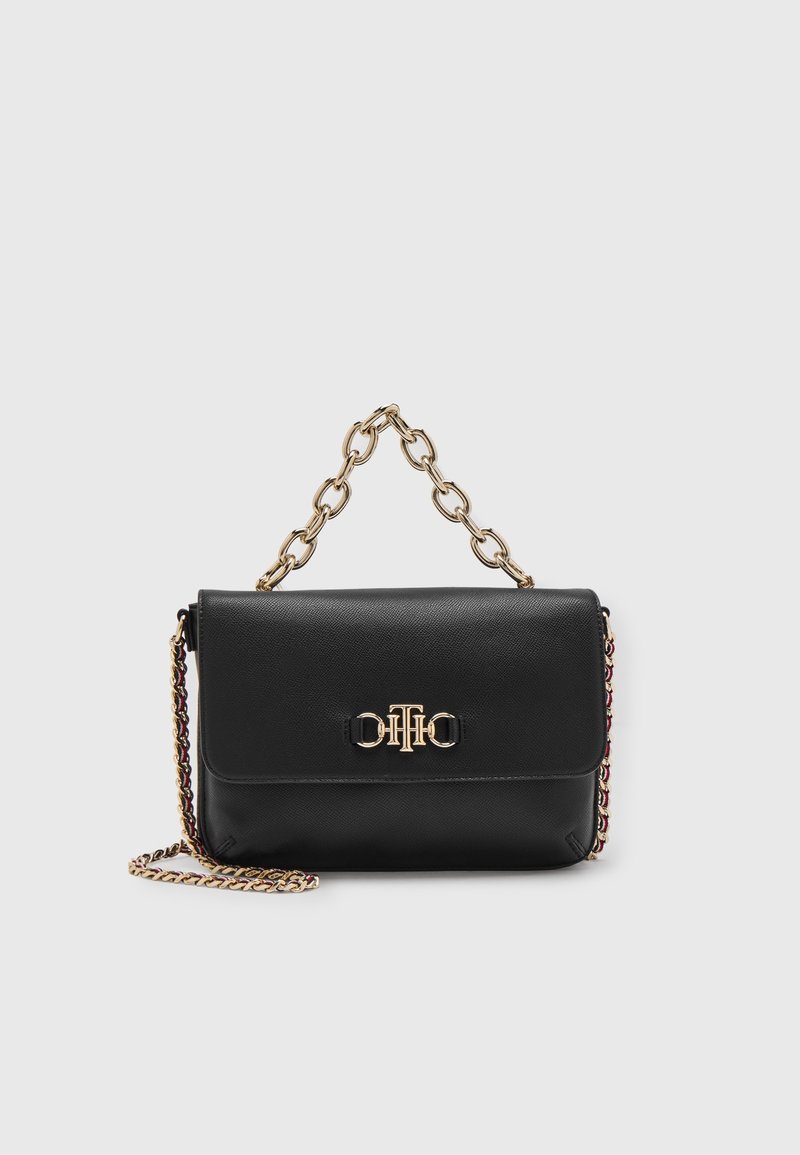 Sac à main en cuir noir avec poignée chaîne dorée et détail du logo sur le rabat avant, posé sur un fond clair uni.
