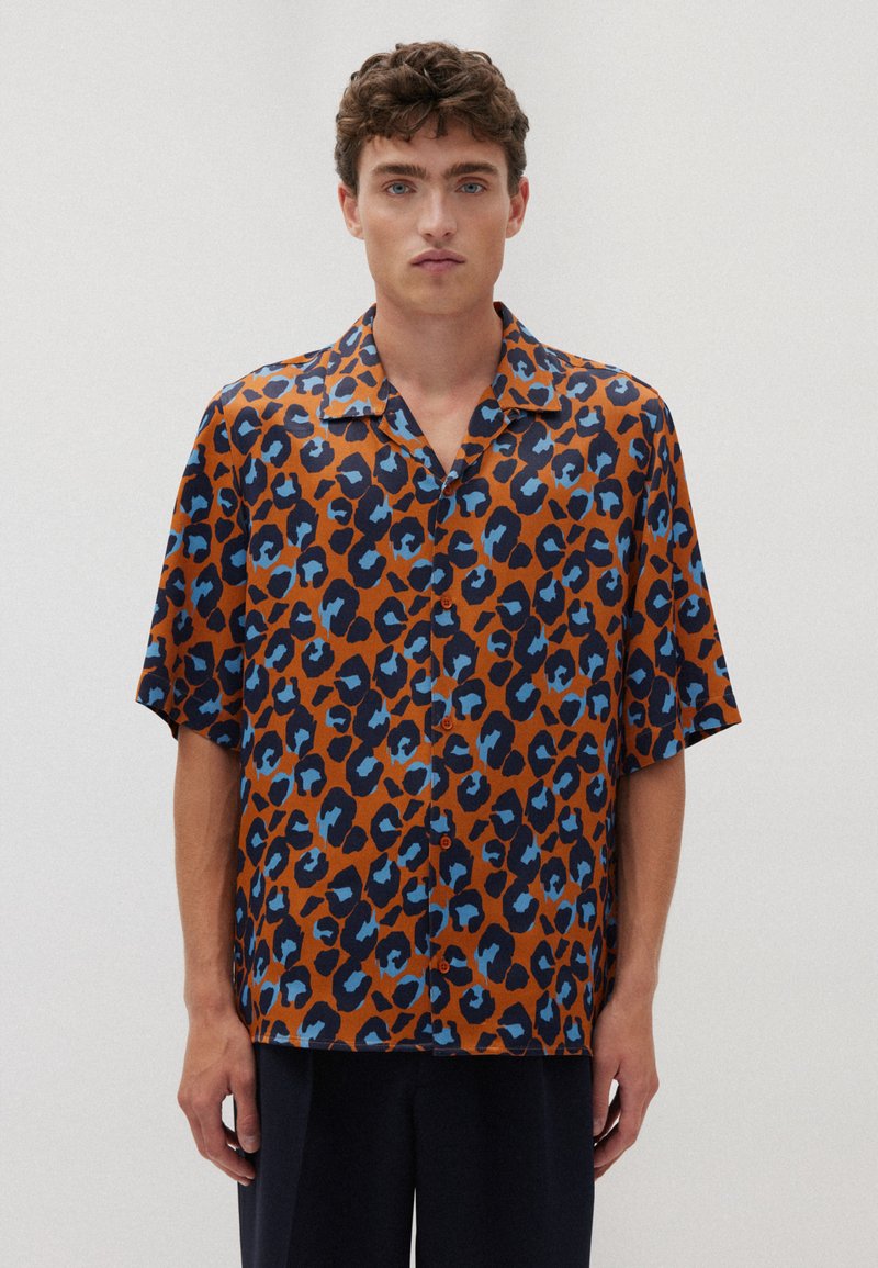 Camicia marrone a maniche corte con un motivo stampa leopardo blu e nero, dotata di collo e chiusura frontale con bottoni. Tessuto dalla consistenza liscia.