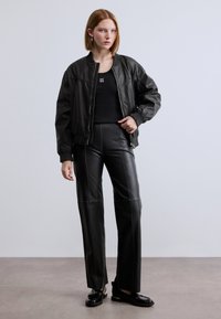 Μαύρο δερμάτινο μπουφάν τύπου μπόμερ με ριμπ μανσέτες, εφαρμοστό μαύρο τοπ και μαύρο δερμάτινο παντελόνι ψηλόμεσο. Μαύρα λοφάρια με χρυσές λεπτομέρειες.