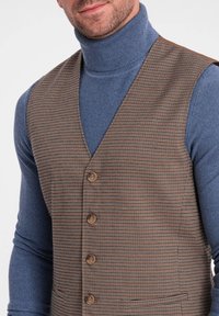 Braunes Hahnentrittmuster-Weste mit fünf Knöpfen und Reverskragen, getragen über einem blauen Rollkragenpullover. Die Textur ist glatt mit einer taillierten Passform.