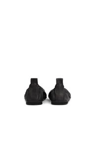 Chaussures plates en cuir noir avec une texture douce, un bout rond et un petit talon, présentant une finition lisse et des détails de couture subtils.