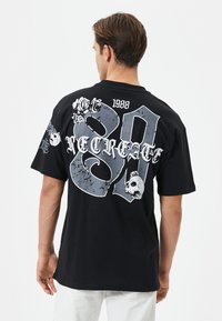 Schwarzes Baumwoll-T-Shirt mit großen grauen Grafiken der Zahlen "80" und "VECREATE", akzentuiert von Rosen und einem Totenkopf, im lässigen Schnitt.