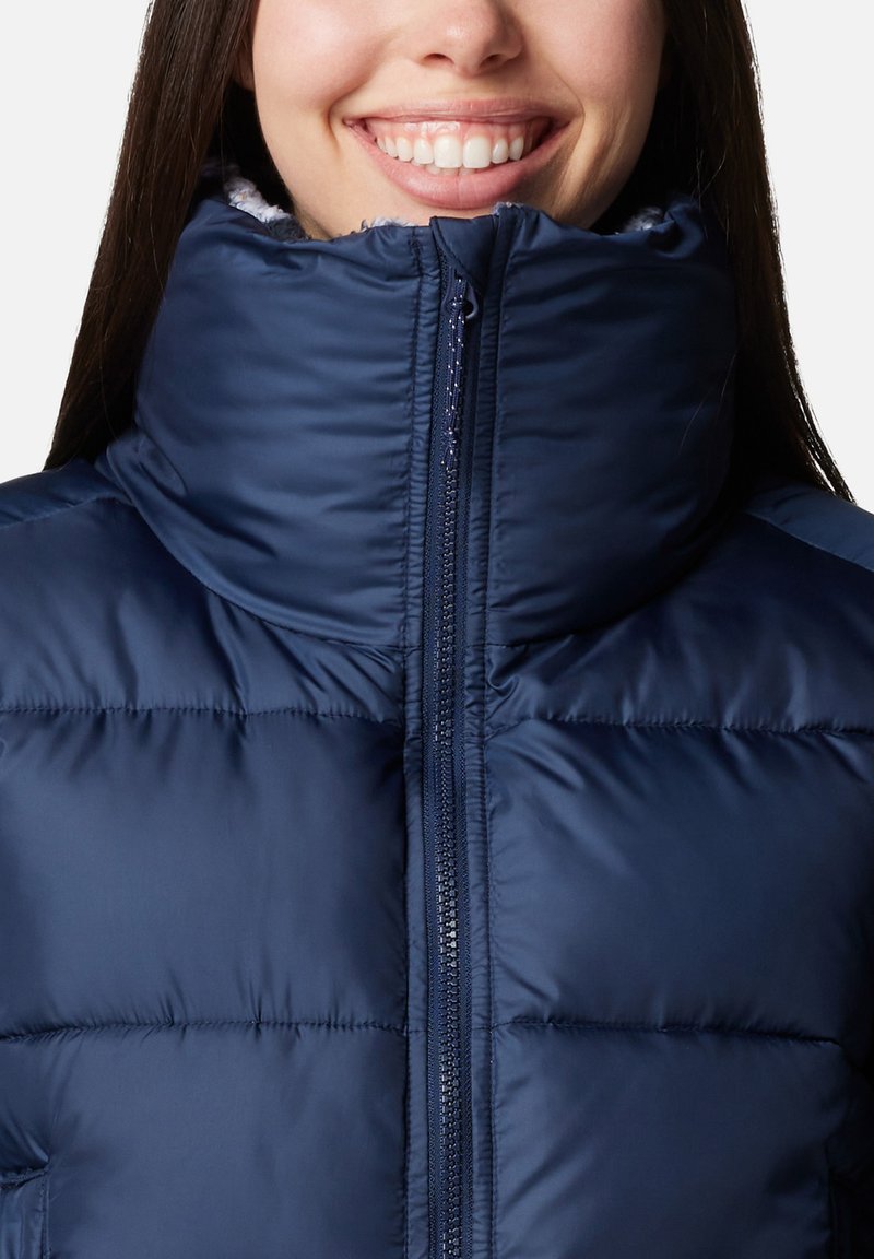 Doudoune bleu marine avec un col haut, fermeture éclair et un design matelassé horizontal. Texture douce et lisse avec un intérieur moelleux.