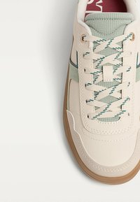 Sneaker with a cream leather upper, mint green accents, and a textured tongue. Features flat laces in stripes and a tan rubber sole.