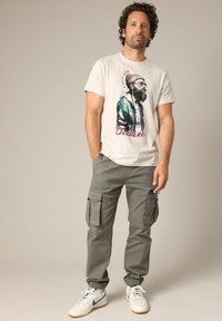 Lichtbeige graphic t-shirt met een bedrukte afbeelding. Gekleed met grijze cargobroek, met meerdere zakken en een taps toelopende pasvorm. Witte sneakers.