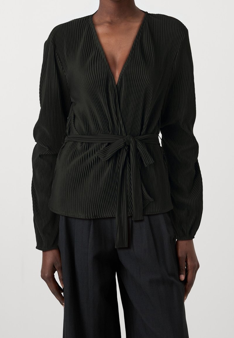Blouse plissée vert foncé avec un décolleté en V profond, manches longues et un détail de ceinture à nouer à la taille. Texture lisse, tissu fluide.