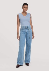 Helles blaues, ärmelloses Top mit V-Ausschnitt, kombiniert mit hoch geschnittenen, weiten hellblauen Jeans, die mit einem gebundenen Gürtel versehen sind.