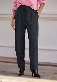 Grå ternede bukser med en afslappet pasform, der har høj talje, sidelommer og en subtil struktur. Kombineret med mørke støvler med hæl.