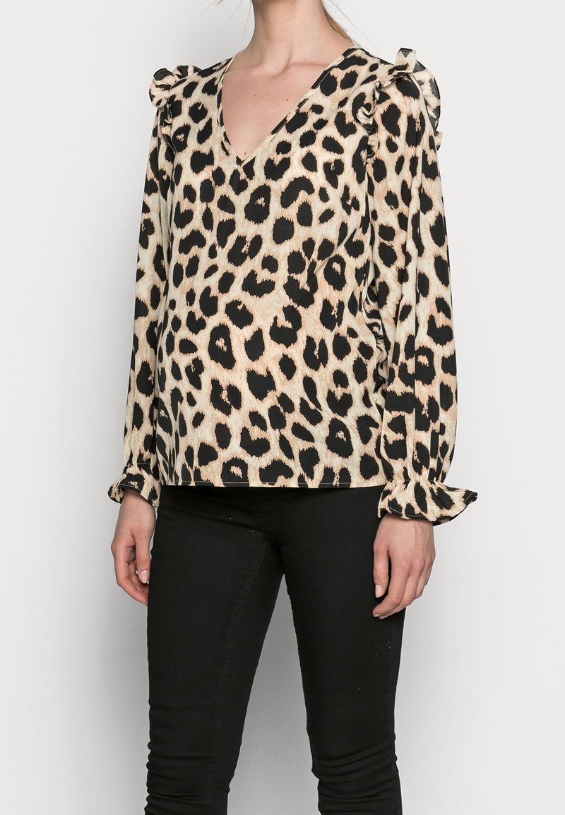 Blouse à imprimé léopard avec col en V, manches froncées et accents volants. Confectionnée dans un tissu lisse, avec des couleurs noir et beige.