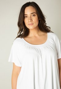 Witte blouse met korte mouwen, een ronde hals en plooidetails op de borst. Gemaakt van zachte, gladde stof. Ontspannen pasvorm.
